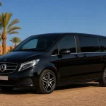 Pristine black Mercedes V-Class luxury passenger van in a palm-lined Marrakech fleet yard
